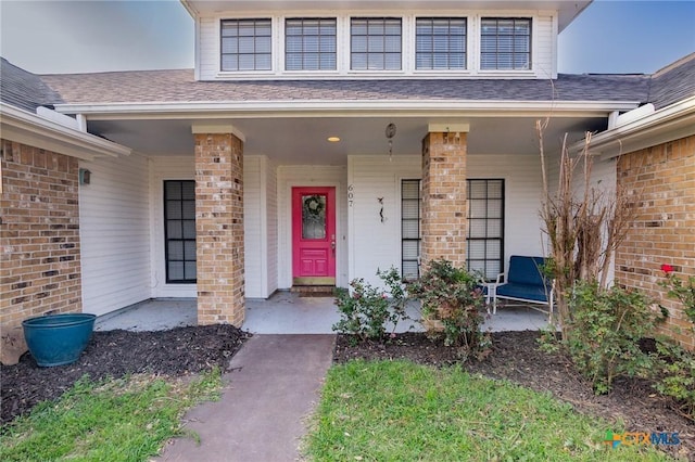 entrance to property with a porch, brick siding, and roof with shingles