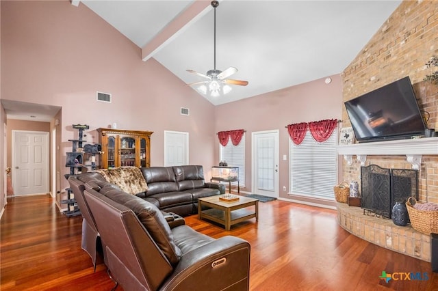 living room with ceiling fan, beamed ceiling, a brick fireplace, and wood finished floors