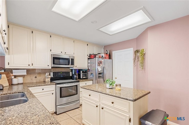 kitchen with a sink, a kitchen island, stainless steel appliances, light tile patterned flooring, and light stone countertops