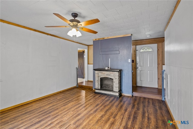 unfurnished living room featuring crown molding, a stone fireplace, dark hardwood / wood-style floors, wood walls, and ceiling fan