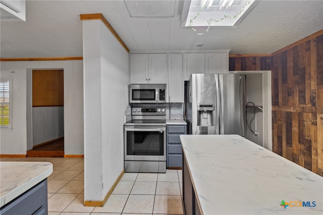 kitchen with stainless steel appliances, wood walls, light tile patterned floors, crown molding, and white cabinetry