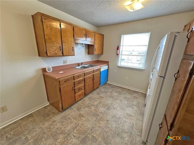 kitchen featuring dishwashing machine, brown cabinetry, a sink, and freestanding refrigerator