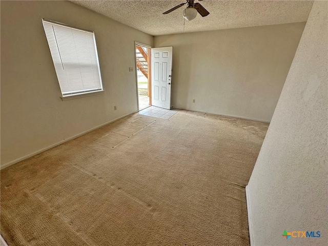 spare room featuring light carpet, baseboards, a ceiling fan, and a textured ceiling