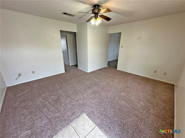 spare room with a textured ceiling, visible vents, carpet, and a ceiling fan