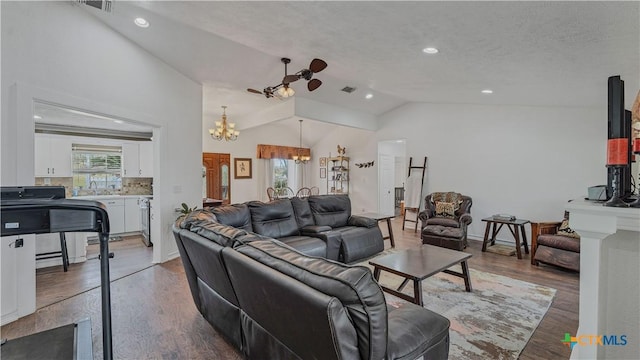 living room with lofted ceiling, dark hardwood / wood-style floors, ceiling fan with notable chandelier, and a textured ceiling