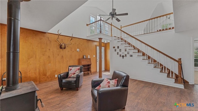 living room featuring high vaulted ceiling, a wood stove, wooden walls, hardwood / wood-style flooring, and ceiling fan