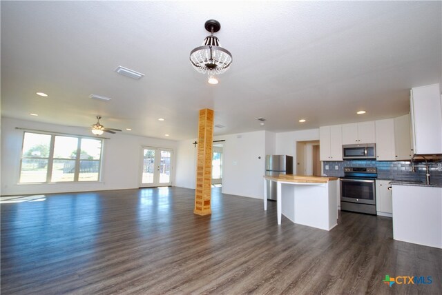 kitchen featuring white cabinetry, hanging light fixtures, dark wood-type flooring, stainless steel appliances, and tasteful backsplash