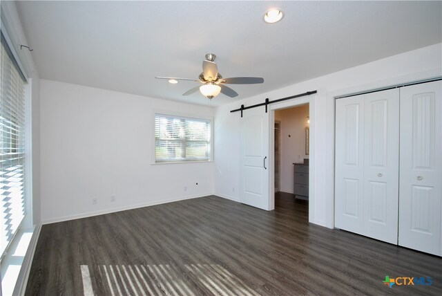 unfurnished bedroom featuring dark hardwood / wood-style flooring, a closet, ceiling fan, and a barn door