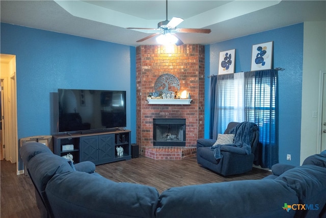 living room featuring a fireplace, hardwood / wood-style floors, a raised ceiling, and ceiling fan