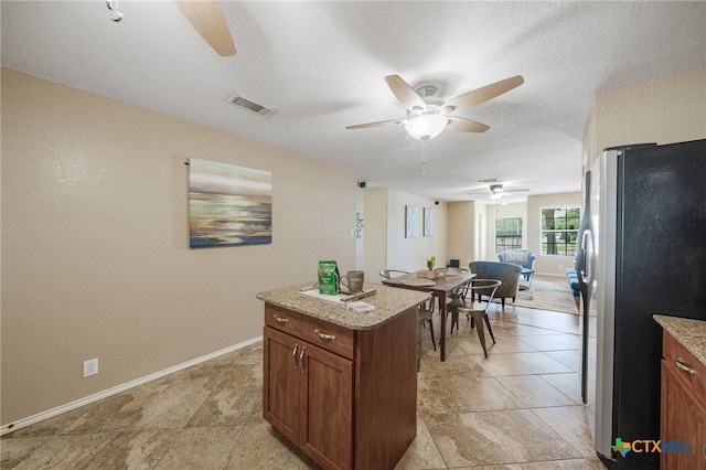 kitchen with a textured ceiling, light tile patterned floors, stainless steel fridge, ceiling fan, and light stone countertops