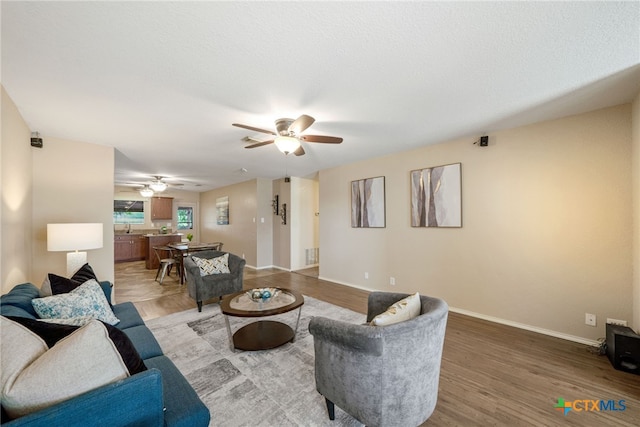 living room featuring ceiling fan, wood-type flooring, sink, and a textured ceiling