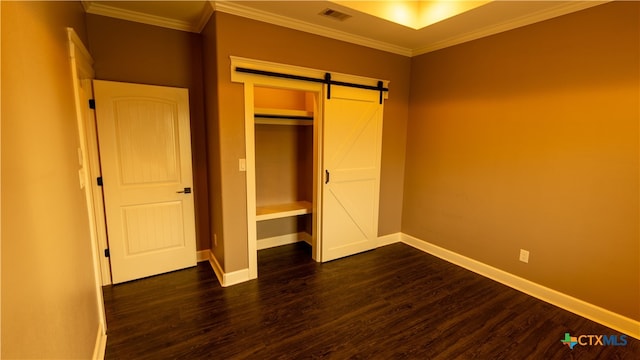 unfurnished bedroom featuring ornamental molding, a barn door, dark hardwood / wood-style flooring, and a closet