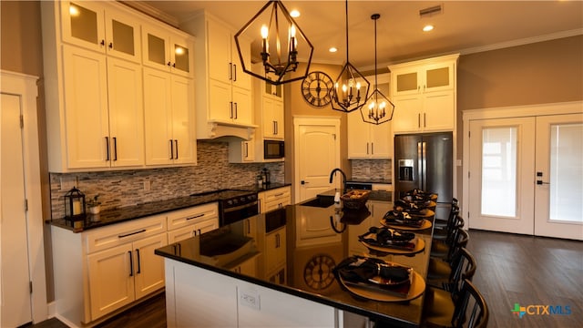 kitchen with an island with sink, black microwave, stainless steel fridge, hanging light fixtures, and french doors