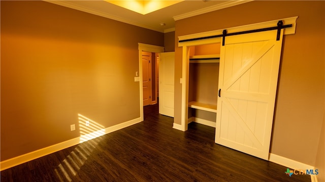 unfurnished bedroom featuring dark wood-type flooring, ornamental molding, a barn door, and a closet