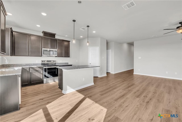 kitchen with light stone countertops, appliances with stainless steel finishes, ceiling fan, pendant lighting, and a kitchen island