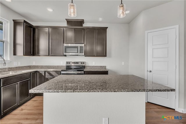 kitchen with decorative light fixtures, a kitchen island, appliances with stainless steel finishes, and dark stone counters