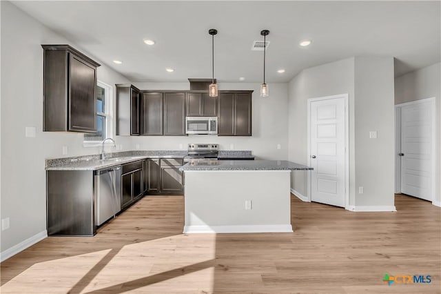 kitchen with a center island, stainless steel appliances, light stone counters, pendant lighting, and light hardwood / wood-style floors