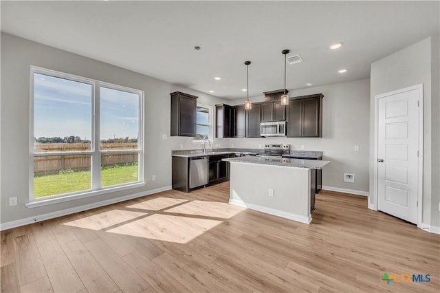 kitchen with pendant lighting, light hardwood / wood-style flooring, appliances with stainless steel finishes, a kitchen island, and light stone counters