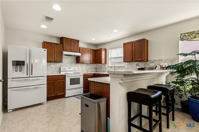 3946 Legend Pond, New Braunfels, TX 78130 - kitchen with white appliances, under cabinet range hood, a peninsula, a kitchen breakfast bar, and light countertops