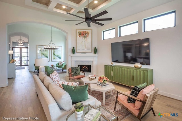 living room featuring beam ceiling, coffered ceiling, wood-type flooring, a healthy amount of sunlight, and a chandelier