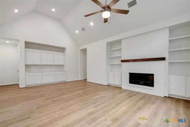 unfurnished living room featuring built in shelves, a brick fireplace, light hardwood / wood-style flooring, and ceiling fan