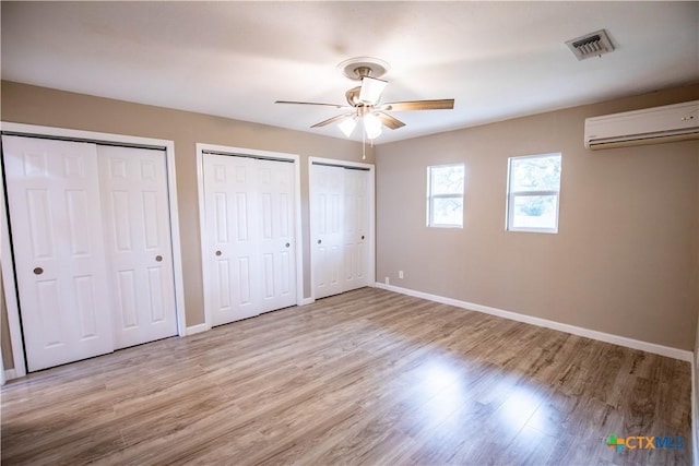 unfurnished bedroom featuring ceiling fan, two closets, light hardwood / wood-style flooring, and an AC wall unit