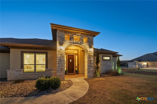 view of front facade featuring stone siding, a shingled roof, and stucco siding