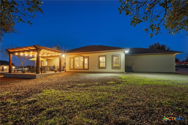 back of house at twilight featuring central AC unit, a chimney, and stucco siding