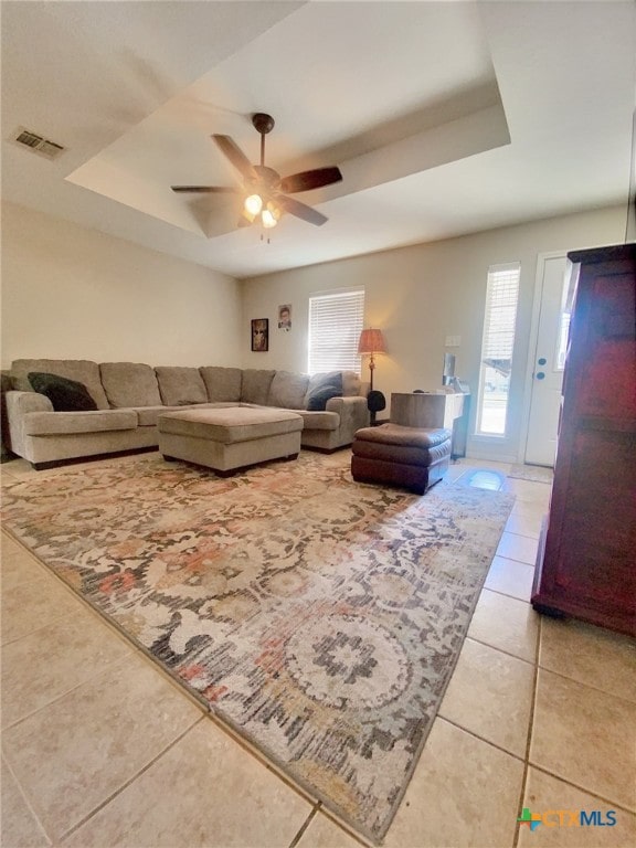 living area with ceiling fan, tile patterned flooring, a raised ceiling, and visible vents