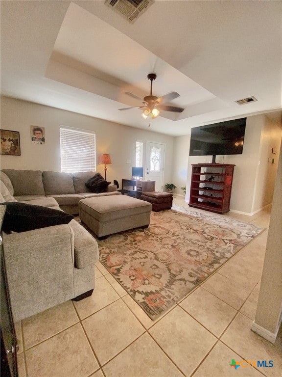 living area featuring visible vents, a tray ceiling, a ceiling fan, and light tile patterned flooring