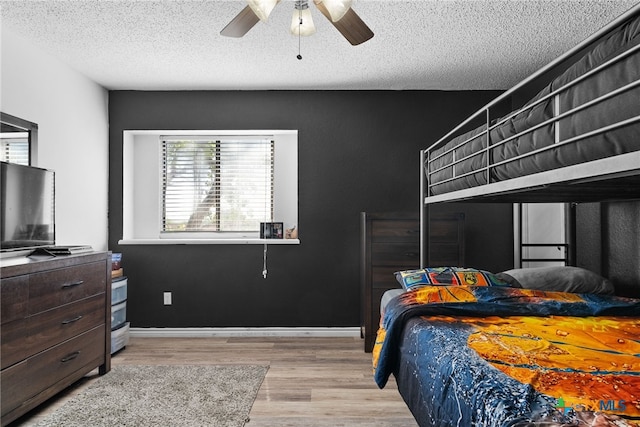 bedroom featuring ceiling fan, multiple windows, light hardwood / wood-style flooring, and a textured ceiling