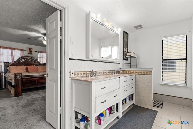 bathroom featuring ceiling fan, a textured ceiling, vanity, tile patterned floors, and tile walls