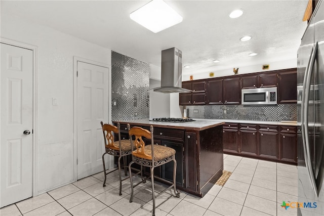 kitchen with light tile patterned flooring, island exhaust hood, dark brown cabinets, and appliances with stainless steel finishes