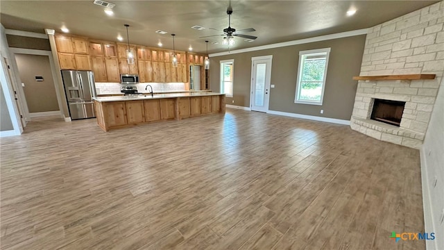 kitchen with a kitchen island with sink, ornamental molding, pendant lighting, light wood-type flooring, and appliances with stainless steel finishes