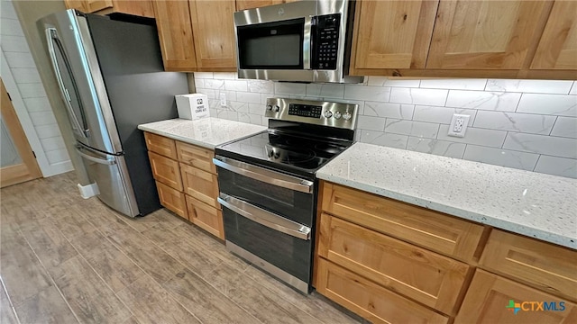 kitchen with appliances with stainless steel finishes, light hardwood / wood-style floors, light stone counters, and backsplash