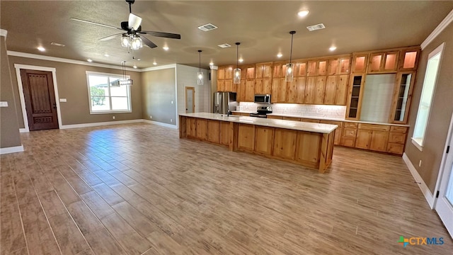 kitchen with a large island with sink, appliances with stainless steel finishes, ceiling fan, light wood-type flooring, and pendant lighting