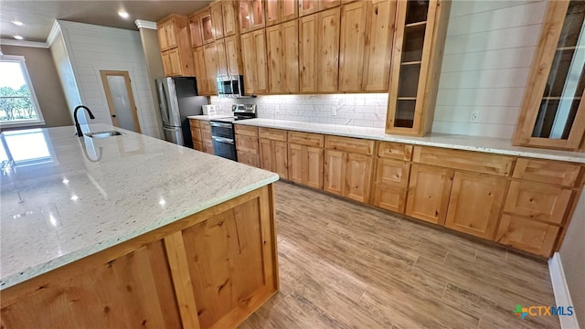 kitchen with stainless steel appliances, sink, light stone countertops, light hardwood / wood-style flooring, and crown molding