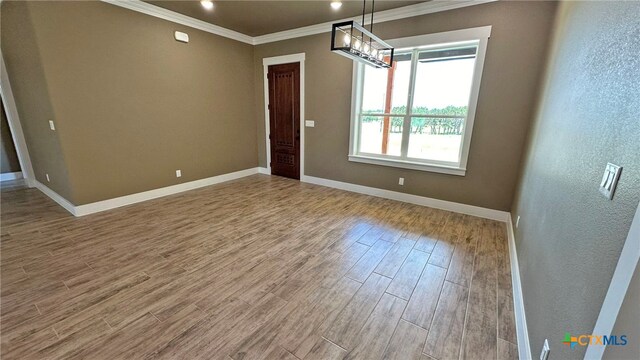 empty room with hardwood / wood-style flooring, a chandelier, and crown molding