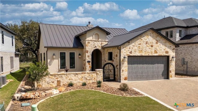 view of front of home with a chimney, metal roof, decorative driveway, an attached garage, and a standing seam roof