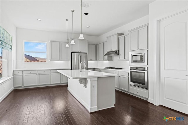 kitchen featuring appliances with stainless steel finishes, a kitchen breakfast bar, dark hardwood / wood-style flooring, pendant lighting, and a kitchen island with sink