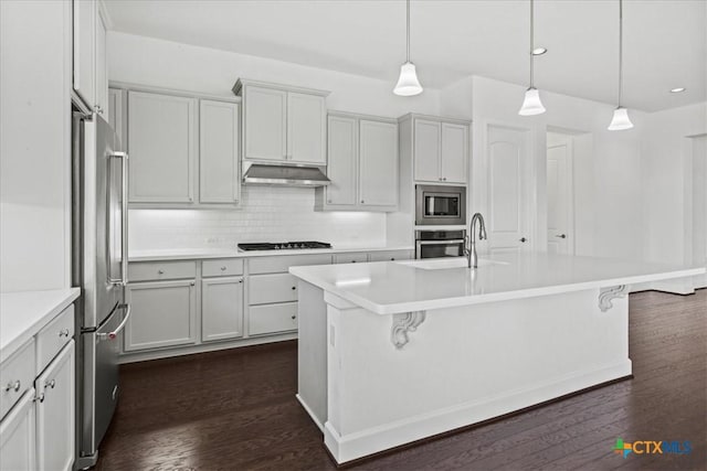 kitchen with stainless steel appliances, hanging light fixtures, and a kitchen island with sink