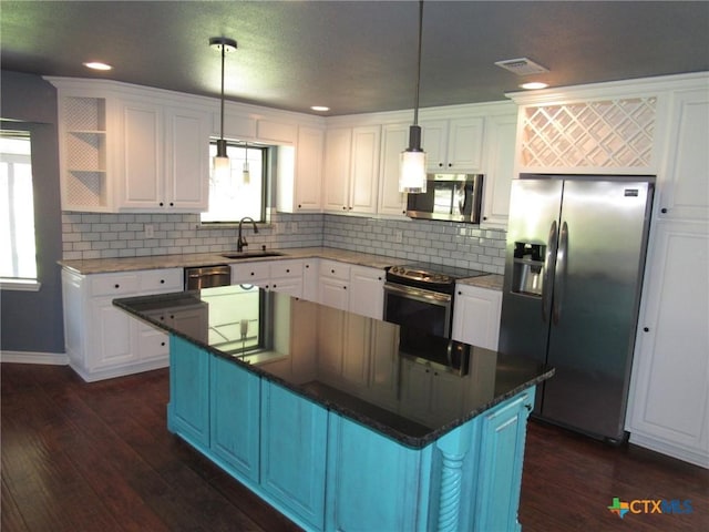 kitchen with sink, hanging light fixtures, stainless steel appliances, white cabinets, and a kitchen island