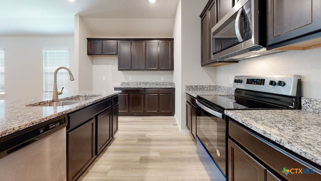 kitchen featuring stainless steel appliances, light stone counters, light hardwood / wood-style floors, and sink