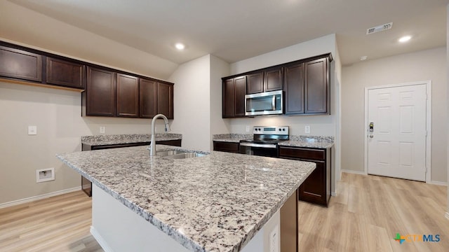 kitchen with appliances with stainless steel finishes, light wood-type flooring, a center island with sink, and sink