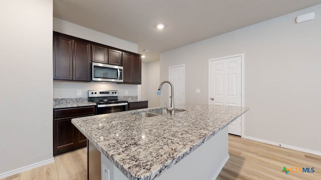 kitchen with light stone countertops, sink, stainless steel appliances, light hardwood / wood-style flooring, and an island with sink