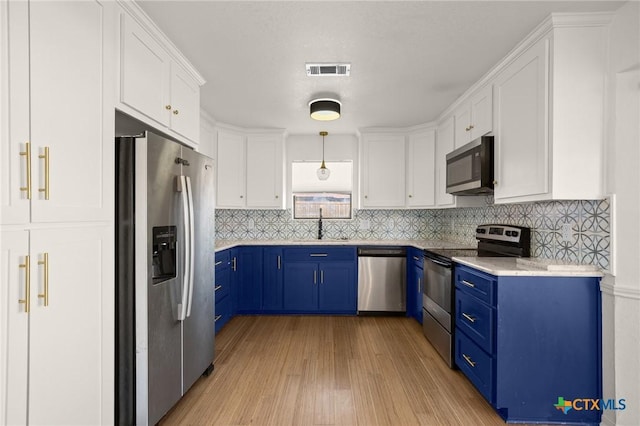 kitchen with appliances with stainless steel finishes, white cabinets, blue cabinets, and decorative light fixtures