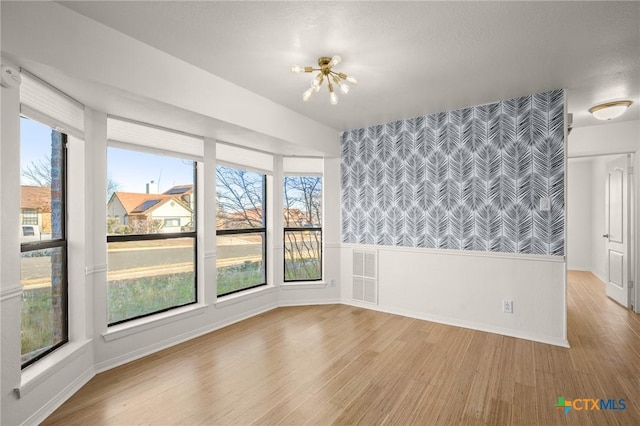 spare room with a healthy amount of sunlight, a notable chandelier, and light hardwood / wood-style flooring