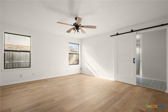 unfurnished room with ceiling fan, light hardwood / wood-style flooring, a barn door, and plenty of natural light