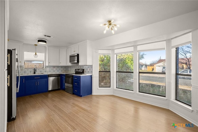 kitchen featuring stainless steel appliances, white cabinetry, blue cabinetry, backsplash, and hanging light fixtures