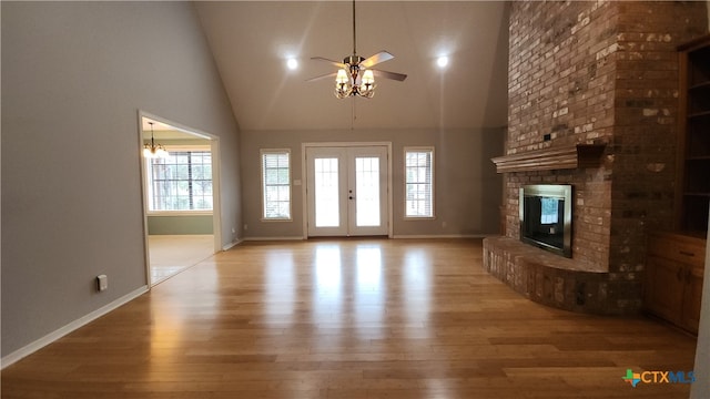 unfurnished living room with high vaulted ceiling, light hardwood / wood-style flooring, a fireplace, and ceiling fan with notable chandelier